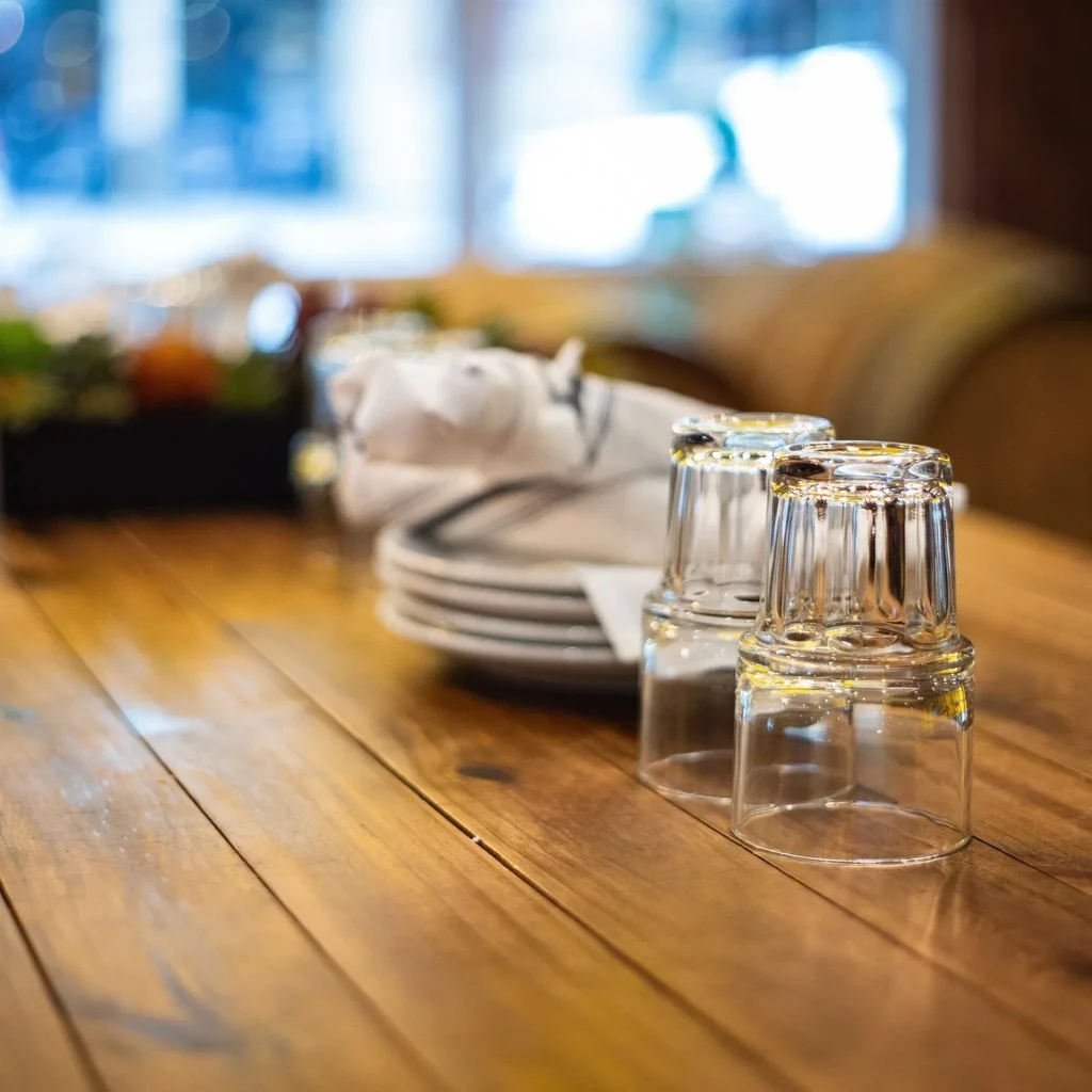Upside-down glasses and stacked plates on a wooden restaurant table.
