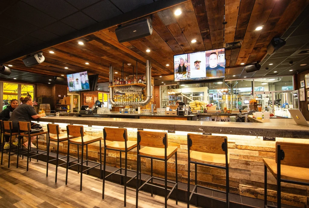 Modern brewpub interior with a long concrete bar and brewing equipment.