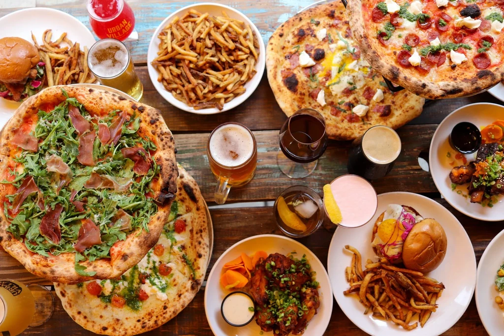 Overhead shot: pizzas, burgers, wings, fries, and various drinks.