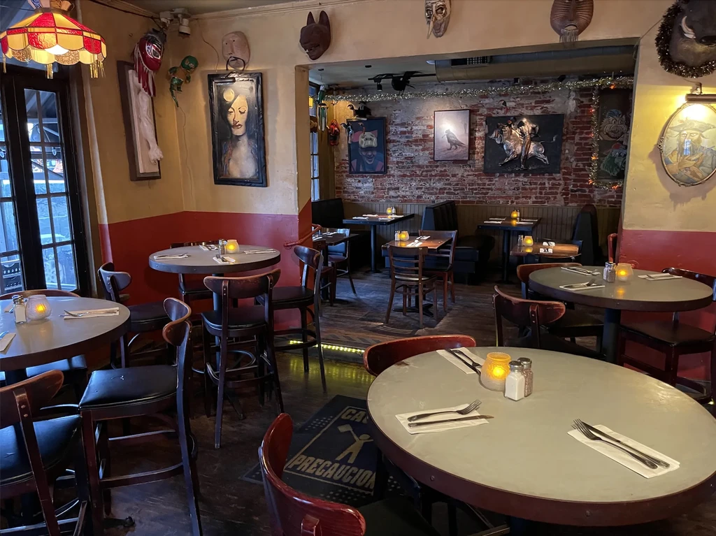 Warmly lit, eclectic restaurant interior with multiple set tables and wall art.