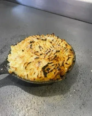 Golden-brown baked dish with mashed potato topping in a cast-iron skillet.