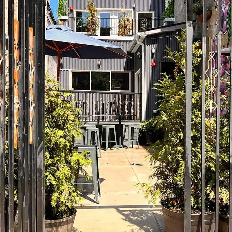 Modern patio with shaded table and building, seen through ornate gate.