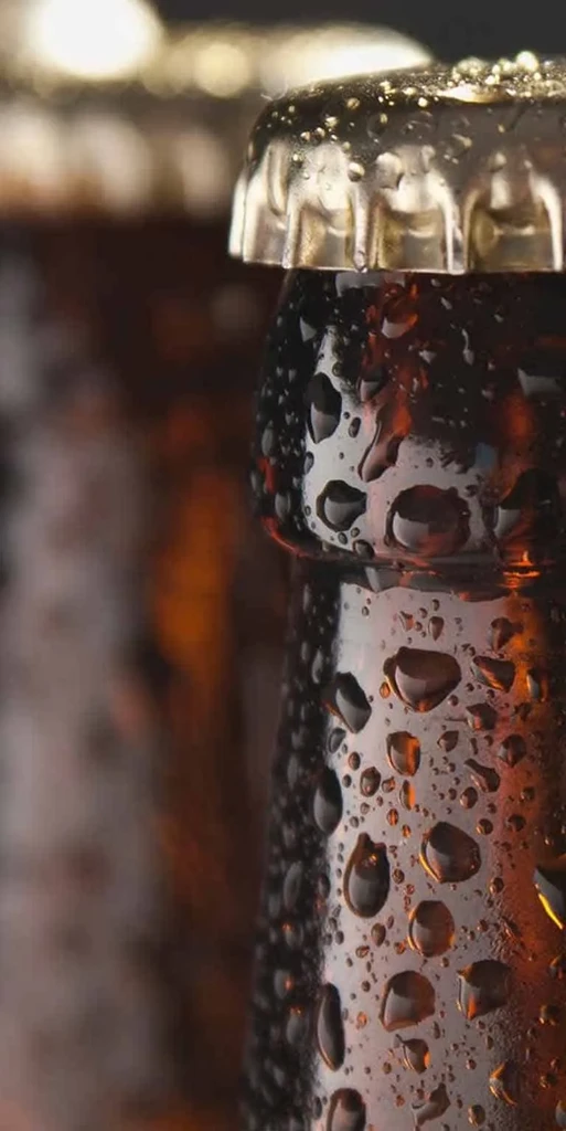 Vertical close-up of a cold, wet amber bottle neck and cap.
