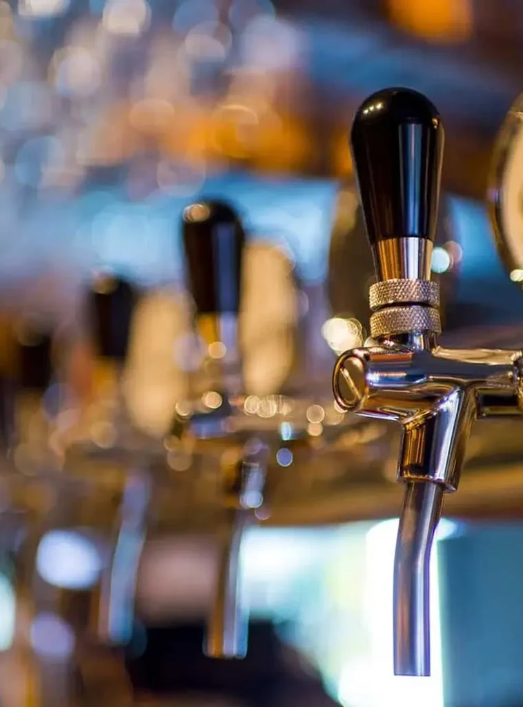 Close-up of a chrome beer tap with blurred taps and lights.