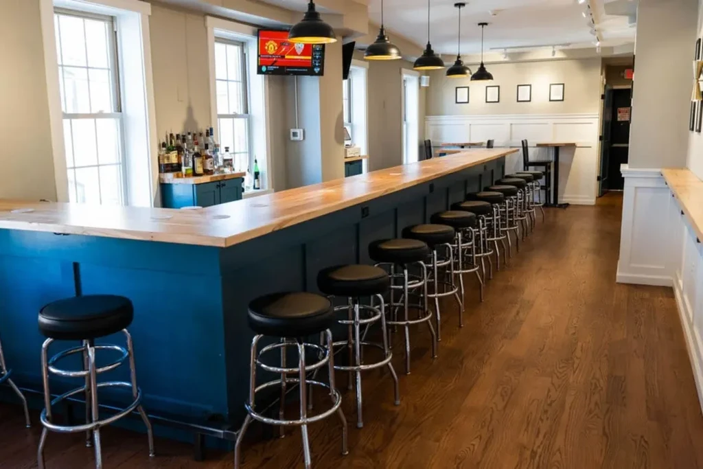 Clean modern bar with teal counter, black stools, and TV showing sports.