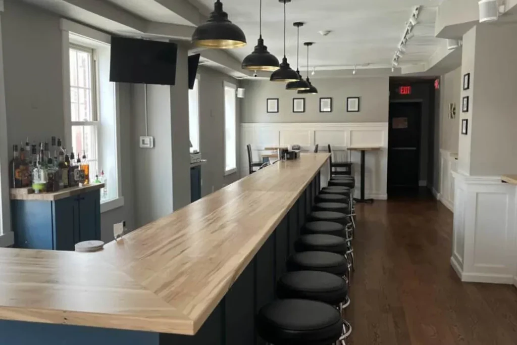 Empty modern bar interior with light wood counter and black stools.