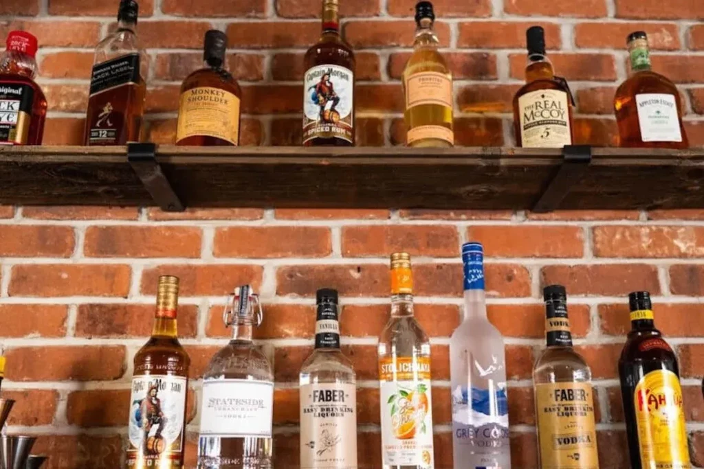 Well-stocked bar shelves display various liquor bottles on a brick wall.