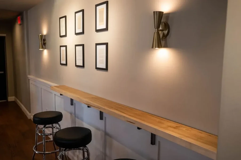 Modern interior with light wood counter, two stools, framed art, and sconces.