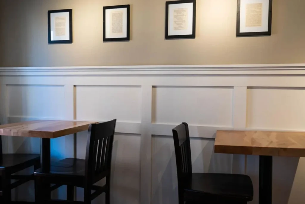 Restaurant interior: wooden tables, dark chairs, wainscoting, and framed wall art.