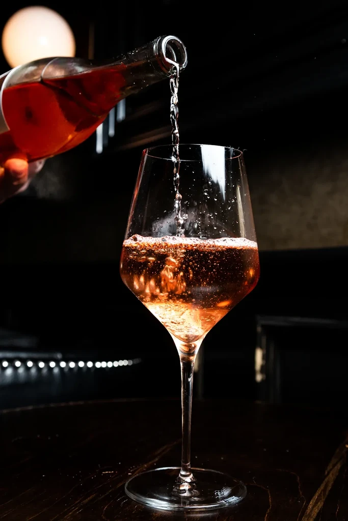 Sparkling pink beverage pours into stemmed wine glass, creating splashes.