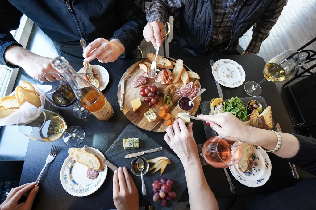 Overhead shot: Multiple hands sharing a charcuterie and cheese board with wine.
