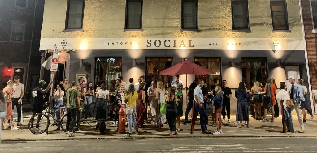 Fishtown Social Wine Café at night, bustling with people on sidewalk.
