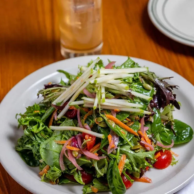 Vibrant mixed green salad with apples, onions, carrots, seeds, tomatoes.