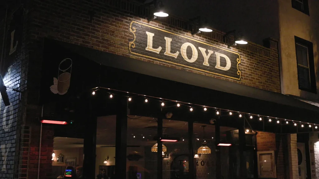 LLOYD bar exterior at night, with illuminated sign, brick, and string lights.