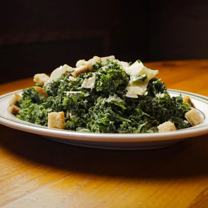 Green kale Caesar salad with croutons and Parmesan, on wood.