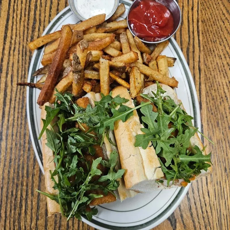Overhead shot: two subs with cutlets and arugula, fries, two sauces.
