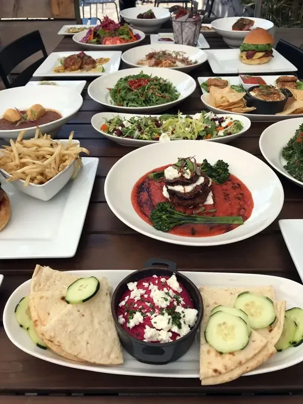 Overhead of a wooden table full of diverse, colorful restaurant dishes.