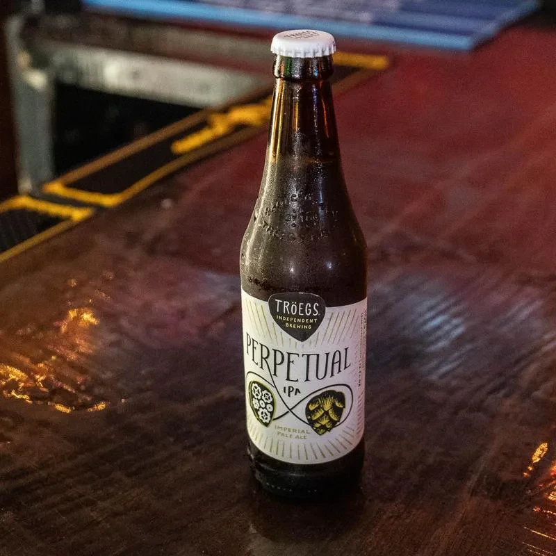 Cold Tröegs Perpetual IPA bottle on a dim wooden bar.