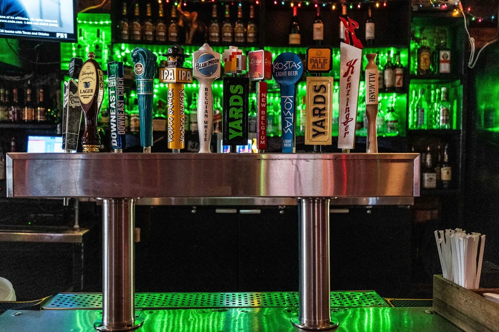 Beer tap handles on a brushed metal structure in a green-lit bar.