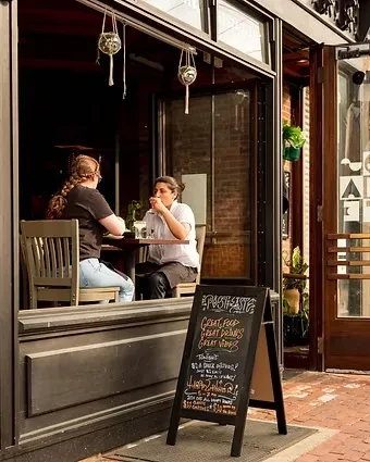Open-front urban restaurant with two women inside and 'PUSHCARTS' chalkboard sign.