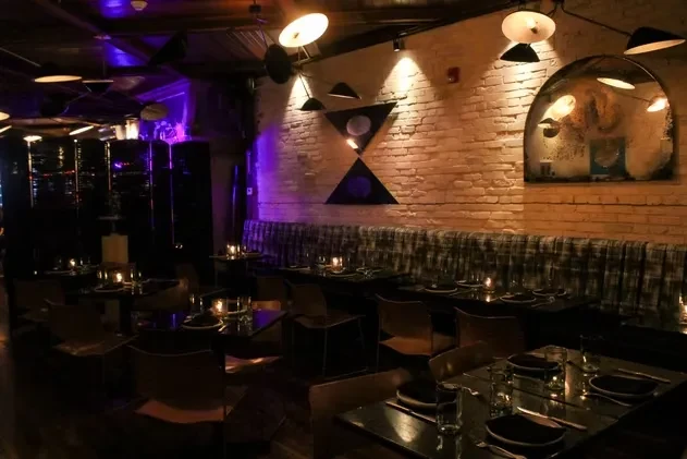 Dark restaurant dining room with brick wall and candlelit tables.