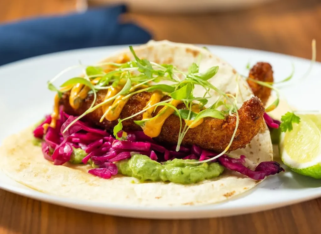 Fried seafood taco with purple cabbage, sauce, microgreens, and lime.