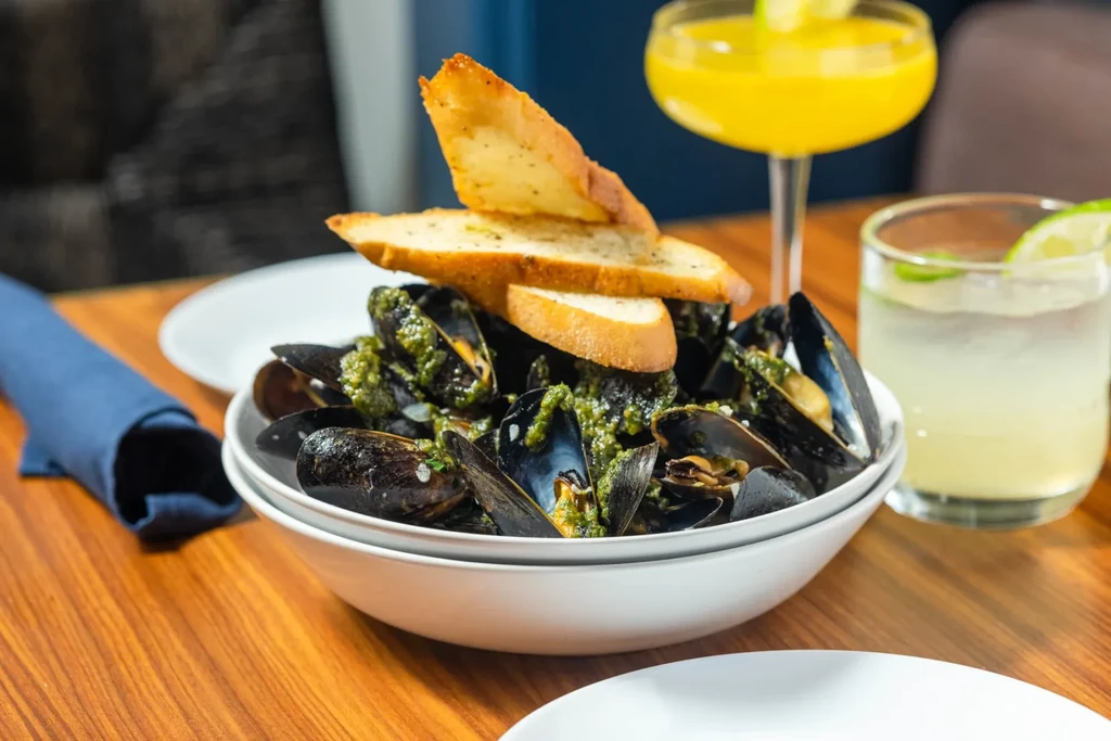 Steamed mussels with green sauce, toasted bread, and two beverages.