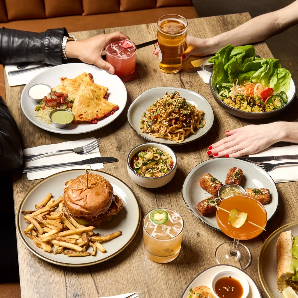High-angle view: hands holding drinks at a table of diverse food.