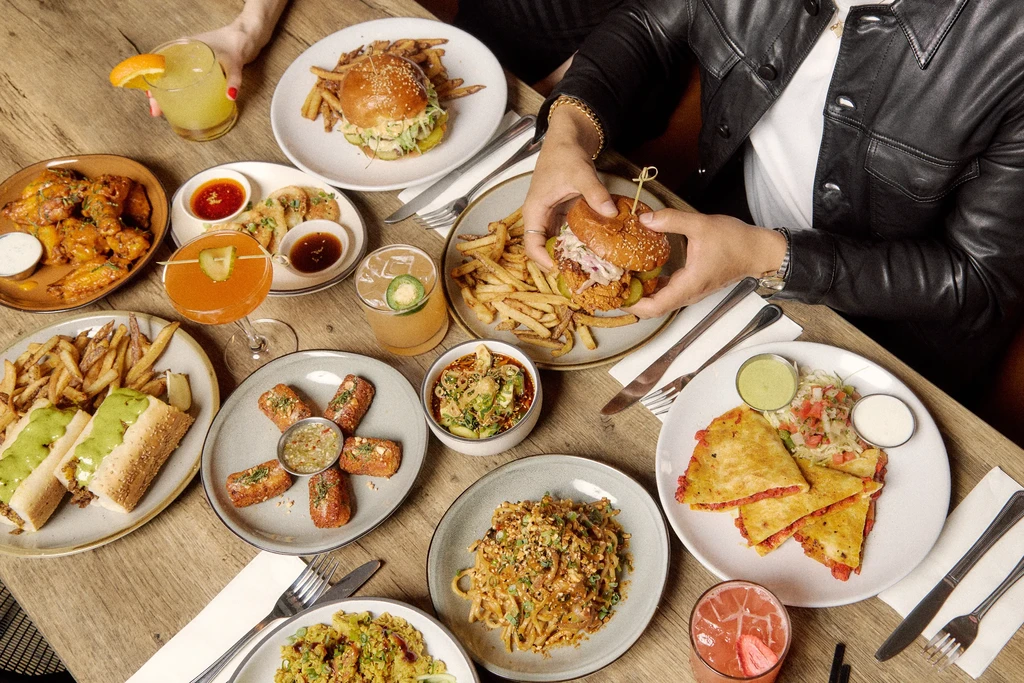 Overhead view of restaurant table with diverse food, drinks, and two hands.