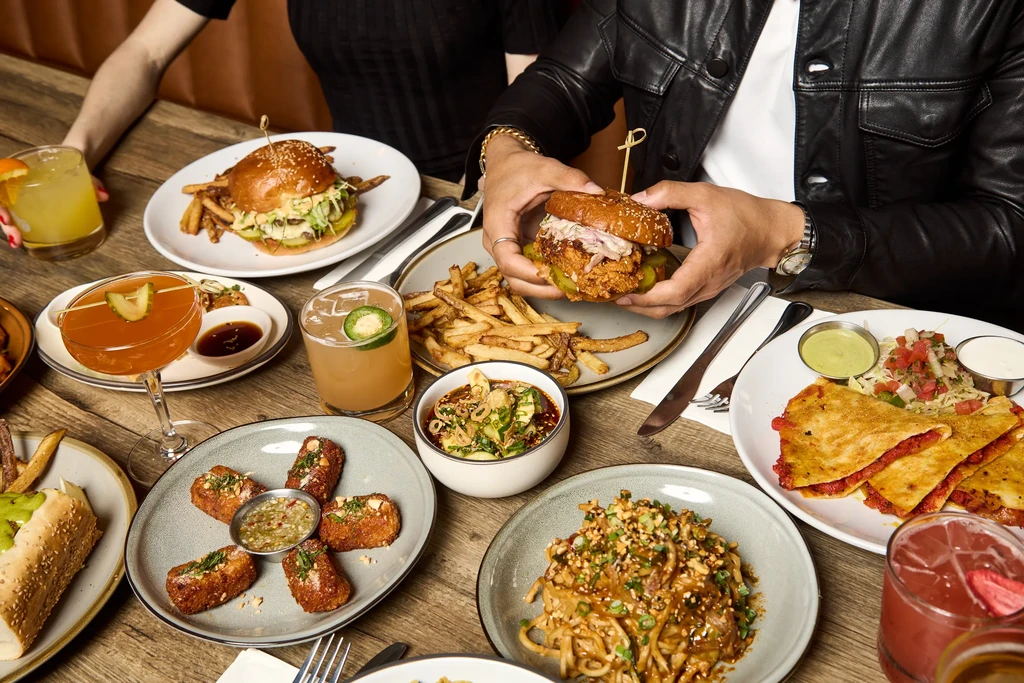 Diverse food and cocktails on a rustic table, with two people dining.