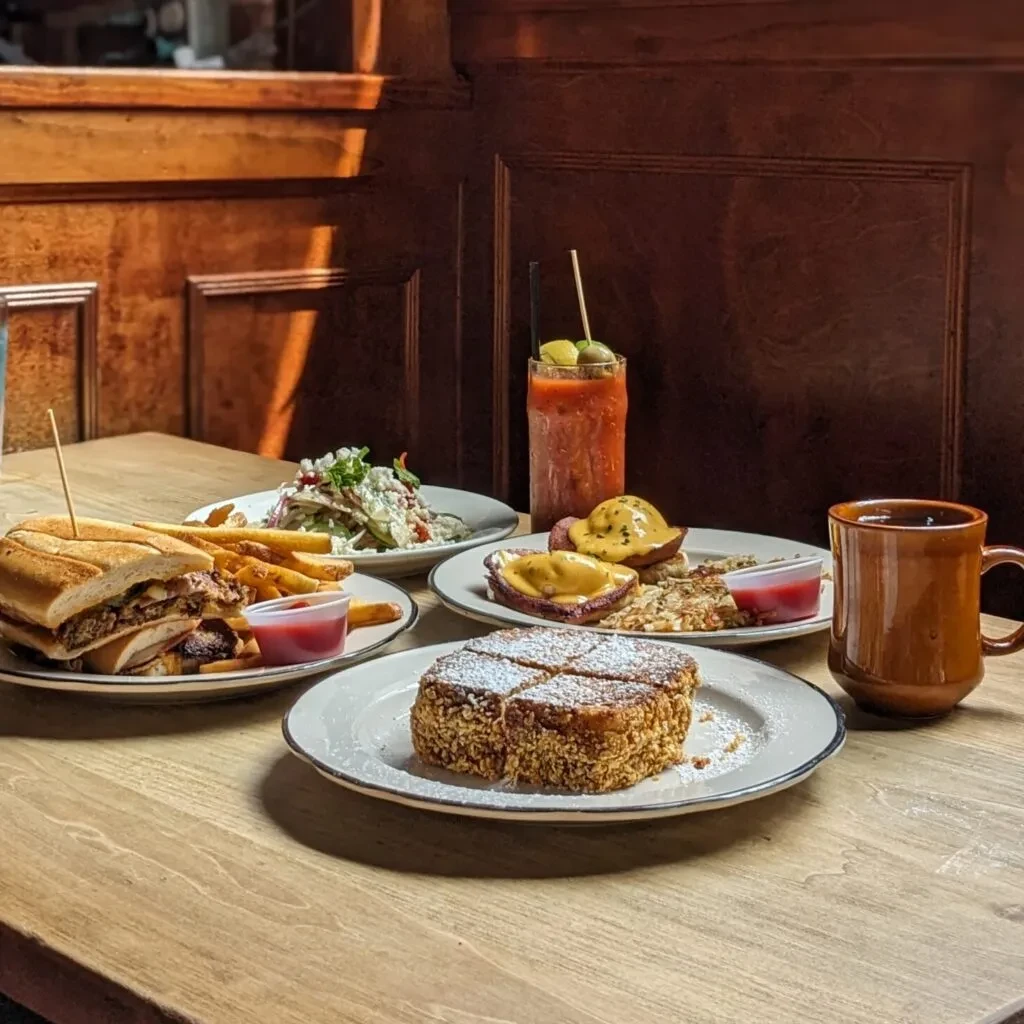 Restaurant table with brunch: sandwich, eggs, French toast, Bloody Mary.