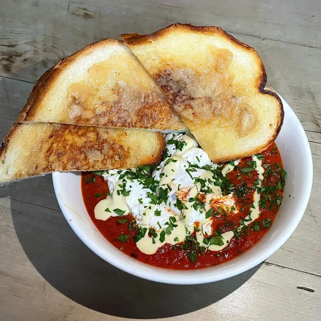 Shakshuka with poached eggs, creamy sauce, fresh herbs, and toast.