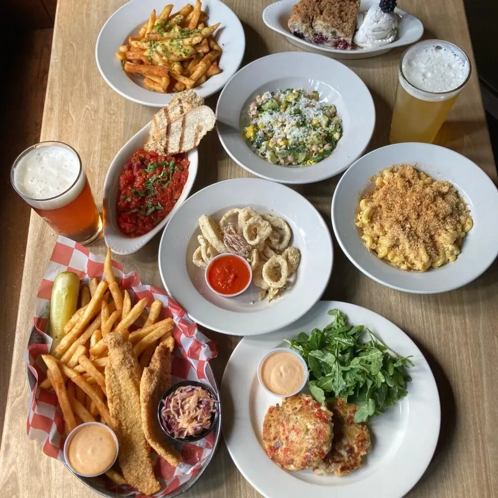 Diverse restaurant dishes and drinks arranged in a flat lay on a wooden table.