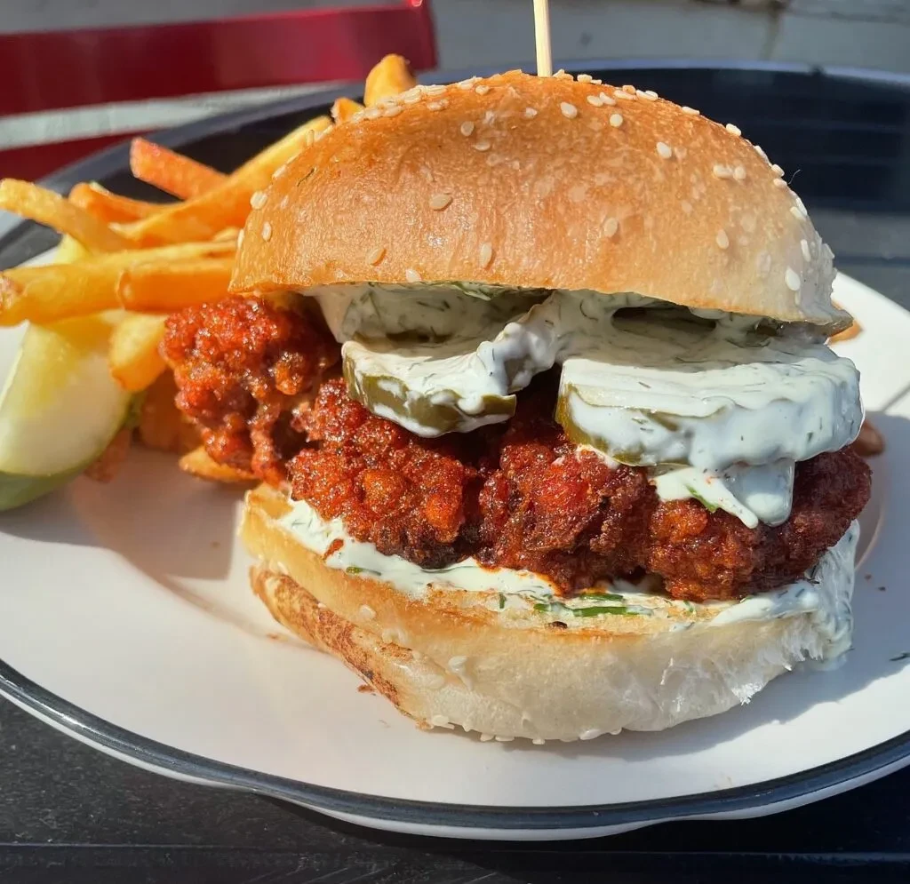 Spicy fried chicken burger with dill pickles, creamy sauce, and fries.
