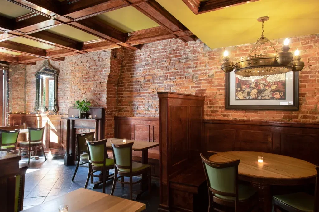 Warm, empty restaurant with brick walls, dark wood, and ornate chandelier.