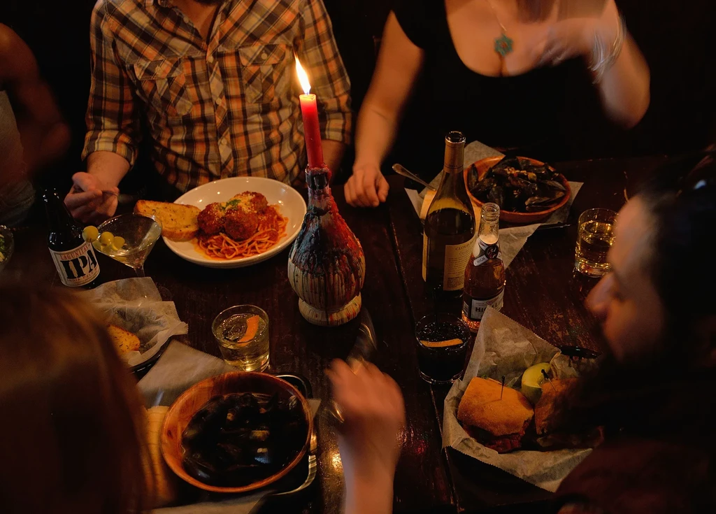Candlelit restaurant table laden with spaghetti, mussels, sandwiches, and drinks.