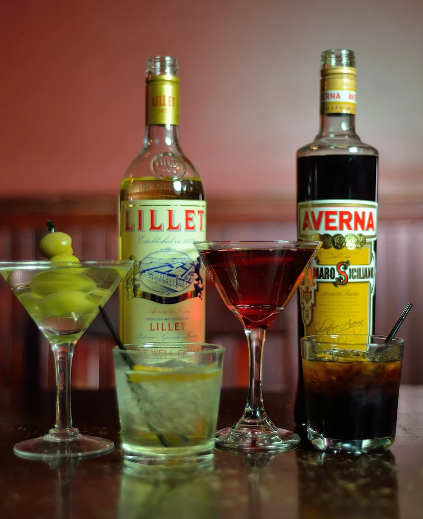 Arrangement of Lillet, Averna, and four cocktails on a reflective surface.