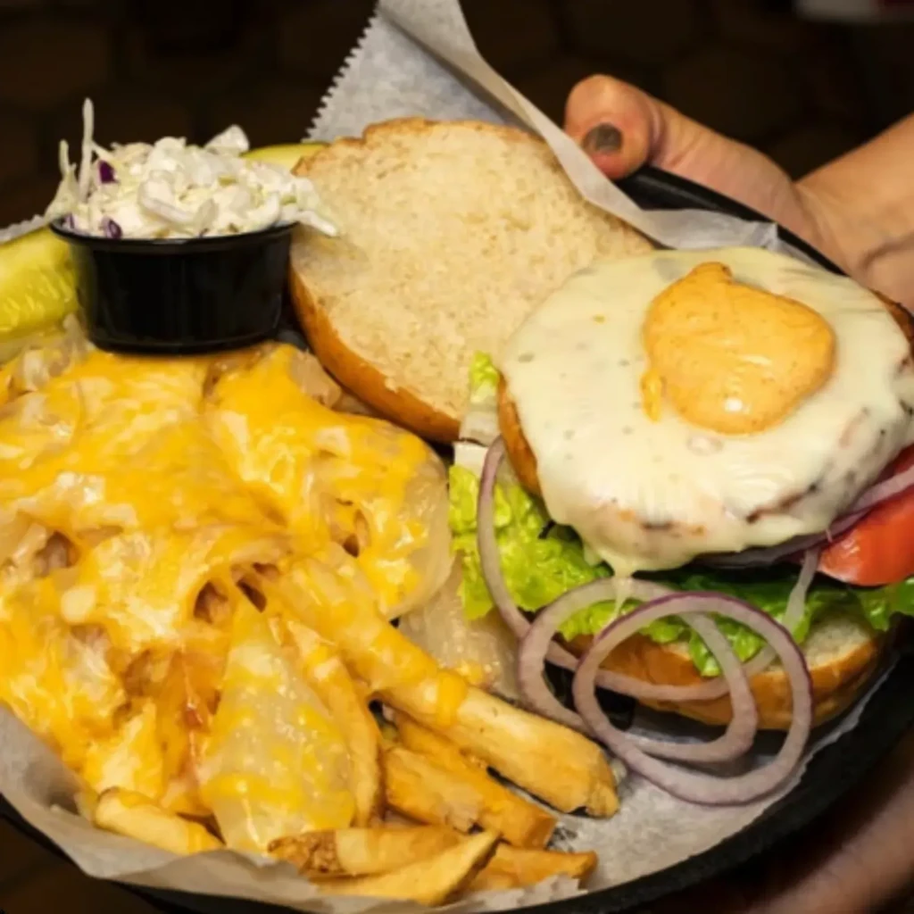 Top-down view: disassembled cheeseburger, cheesy fries, coleslaw, and pickle.
