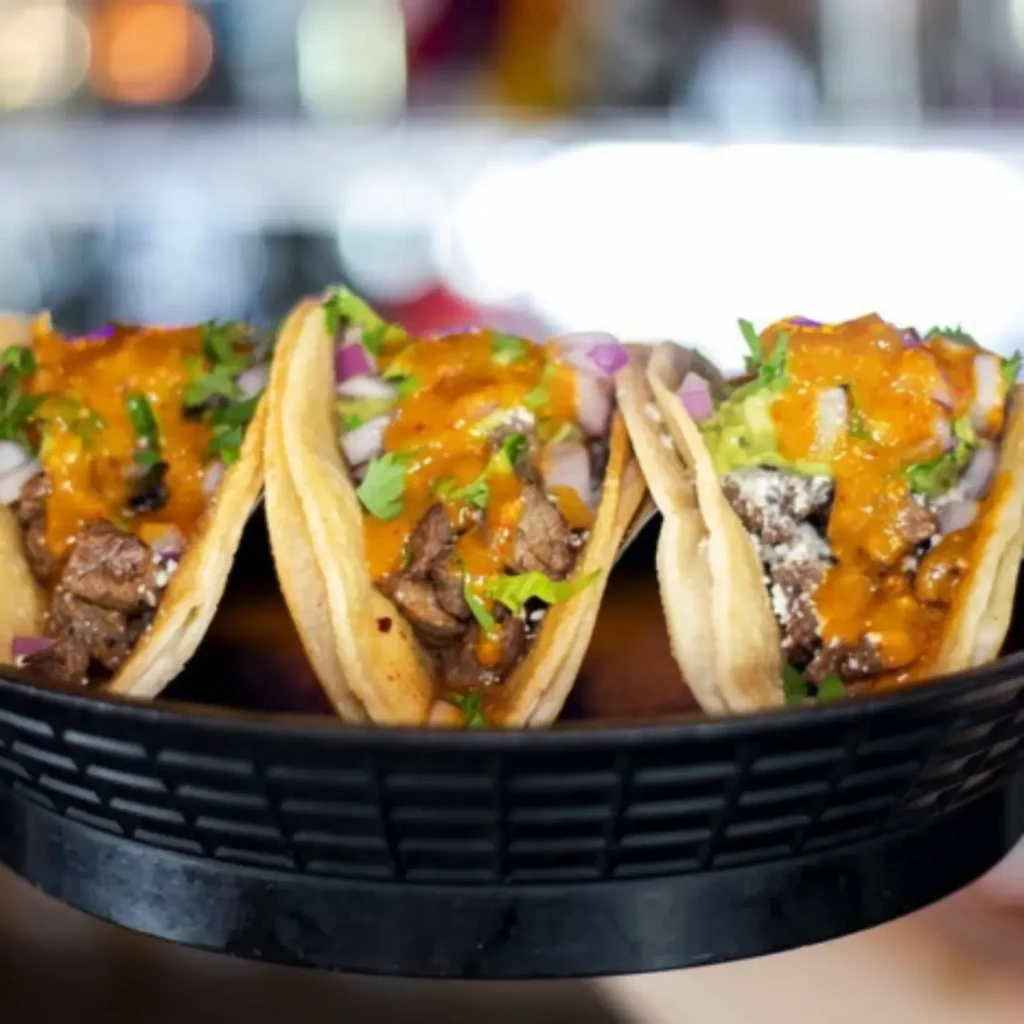 Three grilled meat tacos with sauce, onions, cilantro in a tray.