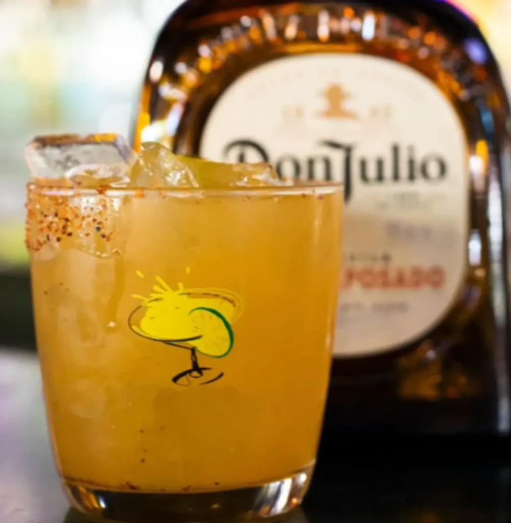 Orange cocktail with chili-spiced rim, lime wedges, and Don Julio tequila.