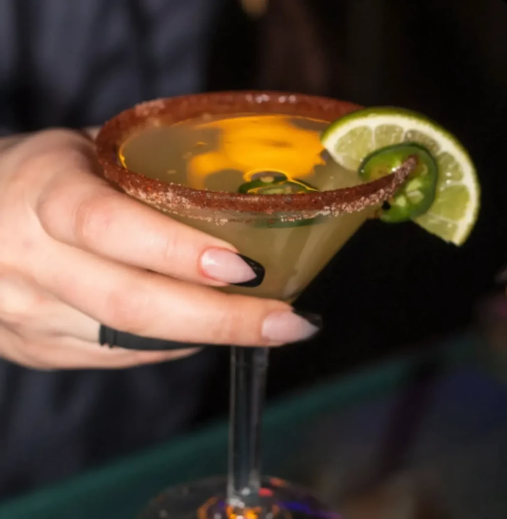 Hand holds a jalapeño cocktail in a tajín-rimmed martini glass.