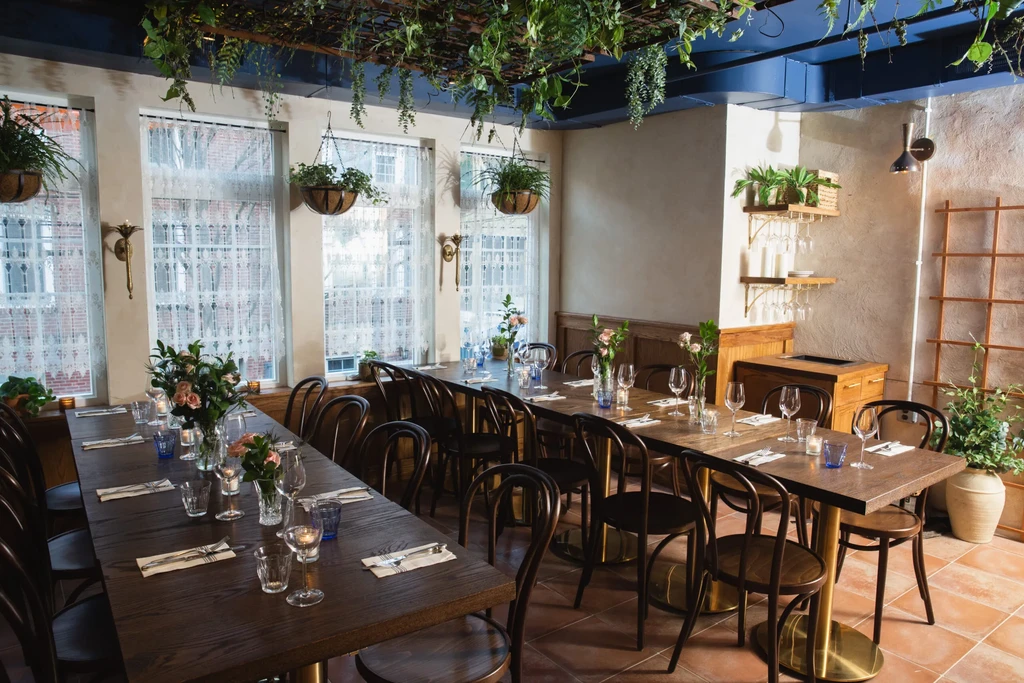 Restaurant dining area with set tables and overhead hanging plants.