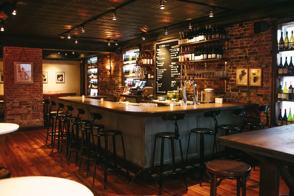 A dimly lit bar with a curved counter, bottle shelves, and chalkboard menu.