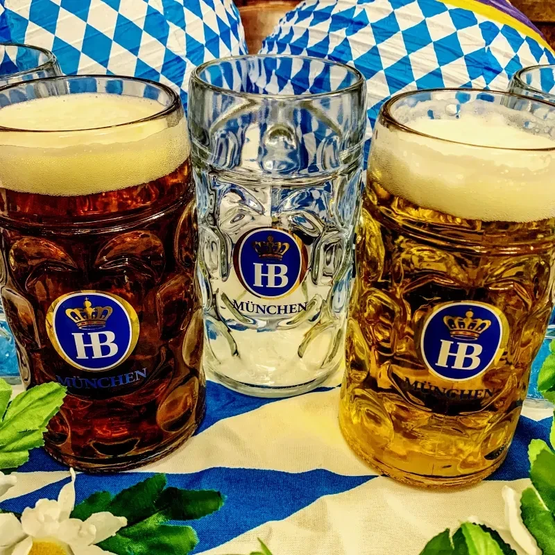 Three Hofbräu München steins, two filled with beer, in a festive setting.