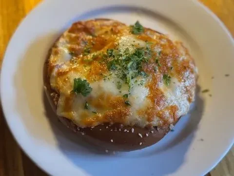 Baked pretzel with bubbly melted cheese and green herbs on a white plate.