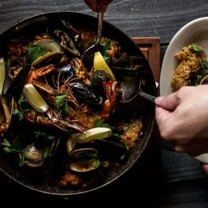 Hands serving vibrant seafood paella with shrimp, mussels, and rice.