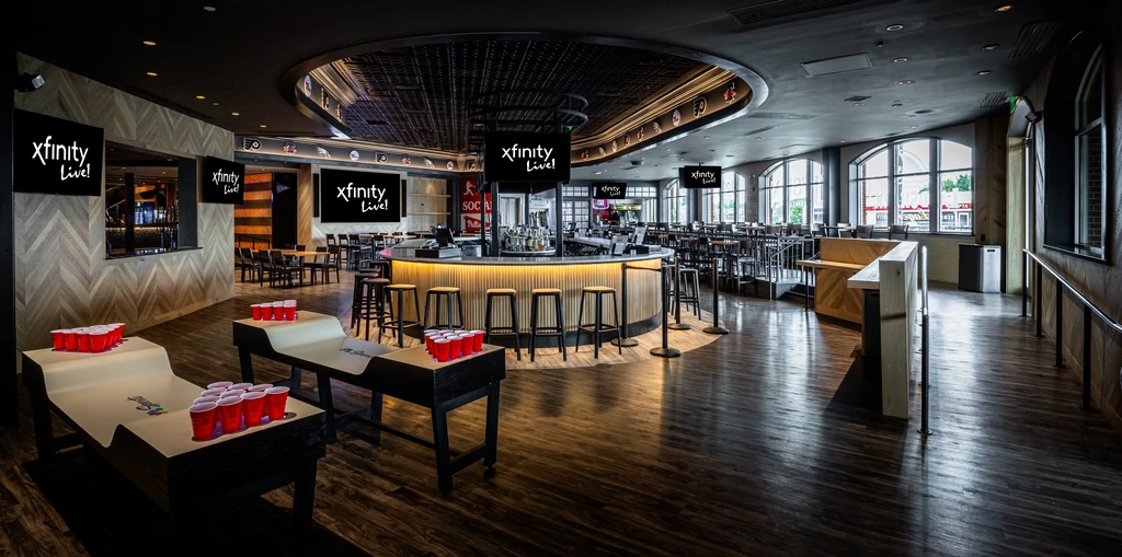 Modern Xfinity Live! sports bar with central bar and beer pong tables.