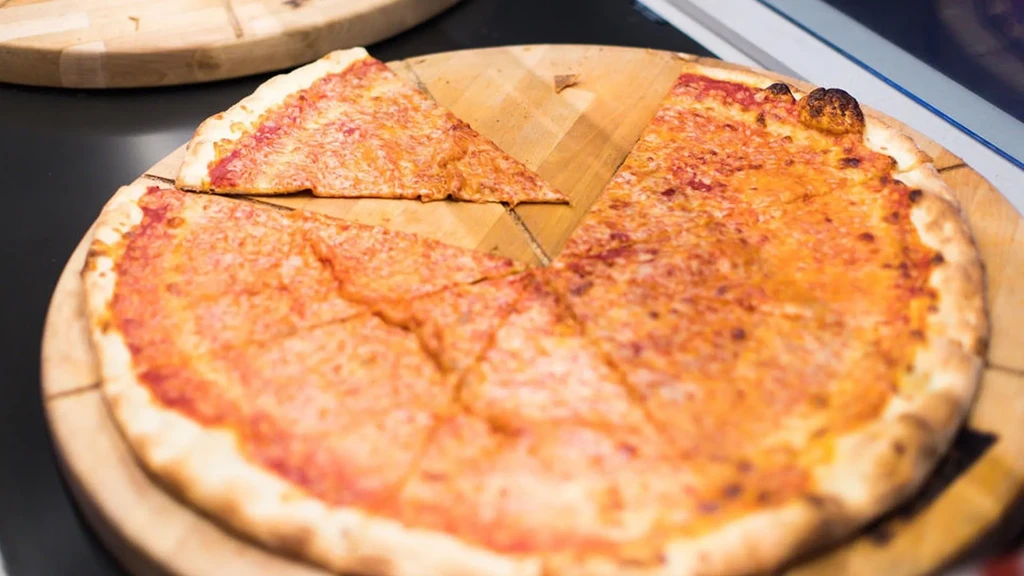 Golden-brown cheese pizza, one slice removed, on a wooden cutting board.