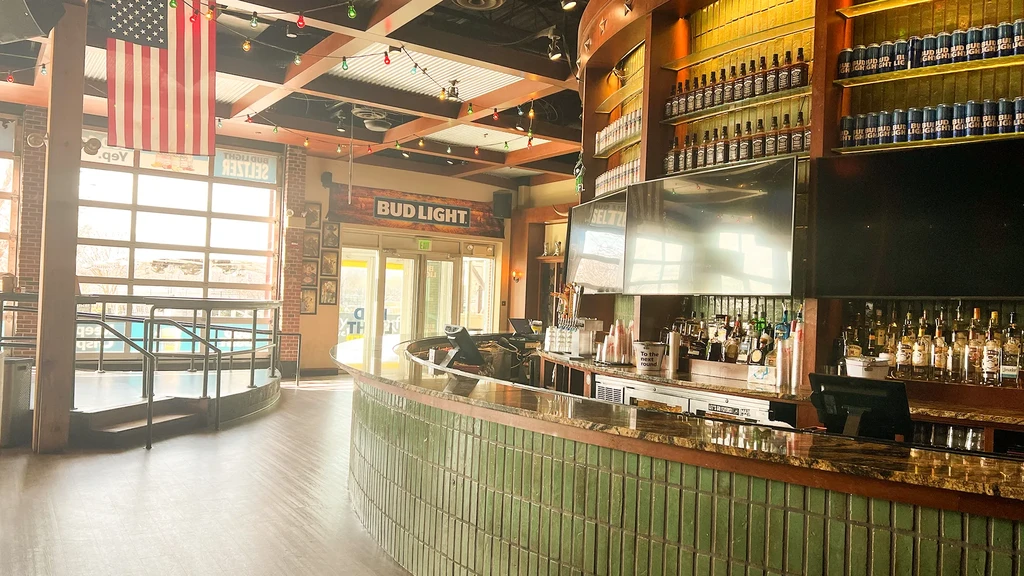 Spacious industrial bar interior features a green-tiled counter and Bud Light.