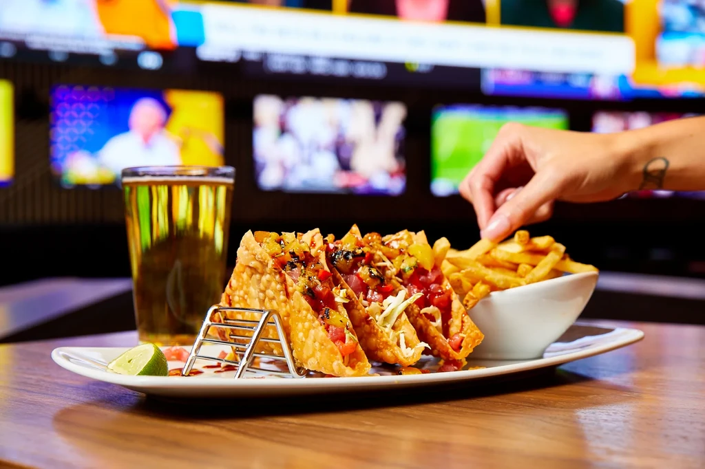 A hand picks a french fry beside mini tacos and beer.